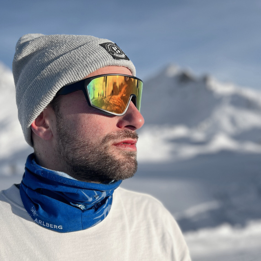 Jongen met een muts en ski zonnebril op die zijn gezocht bedekt. De ski zonnebril heeft rode gepolariseerde spiegelglazen