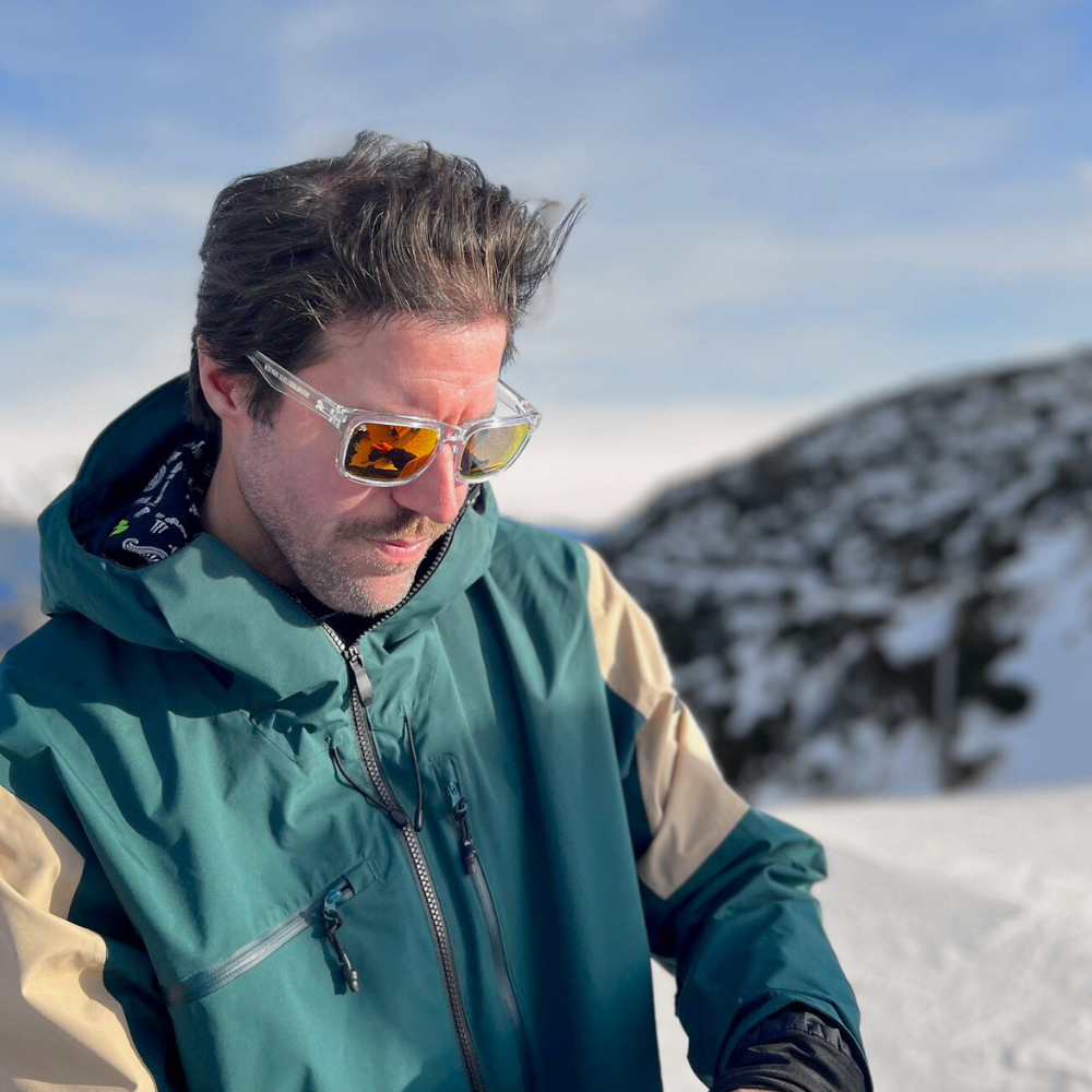 Jongeman in de sneeuw met een transparante ski zonnebril met rode spiegelglazen op.